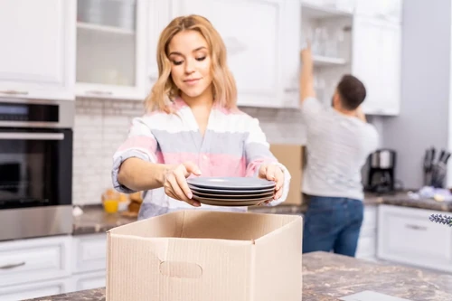 A couple putting kitchen plates and cups into a brown packing box before a move.