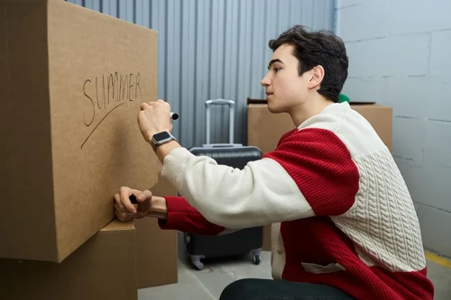 A man packing a storage unit labeling a brown packing box "Summer."